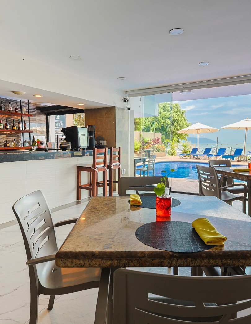Interior de un bar junto a la piscina con mesas y sillas.