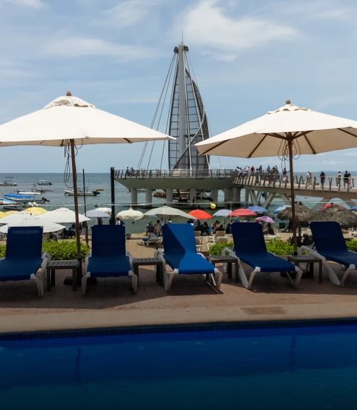 Sillas azules y sombrillas frente al mar, vista de muelle peatonal en la playa.