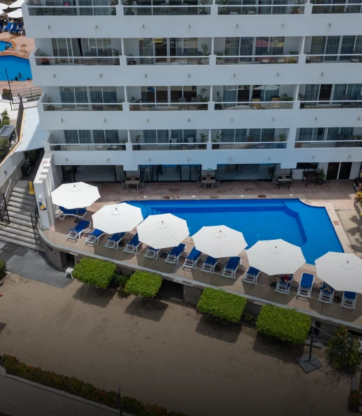 Piscina de hotel con sombrillas y tumbonas vistas desde arriba.
