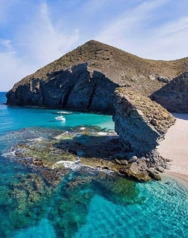 Costa rocosa con agua turquesa y una playa de arena.