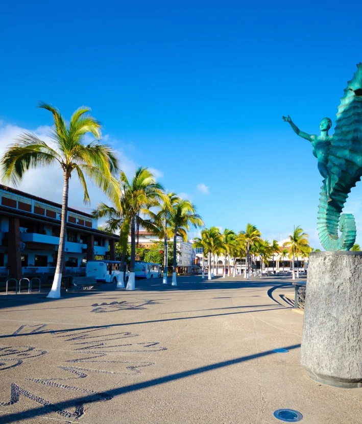 Paseo mar&iacute;timo con palmeras y estatua de bronce a la orilla de la playa.