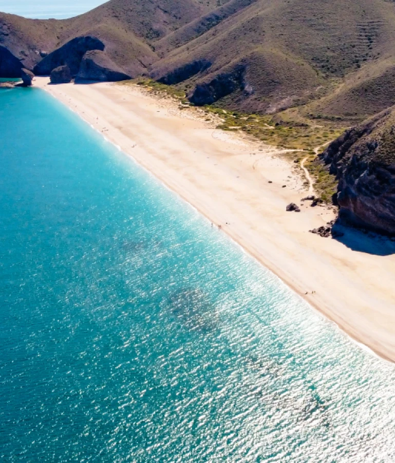 Playa de arena y mar azul con colinas al fondo.