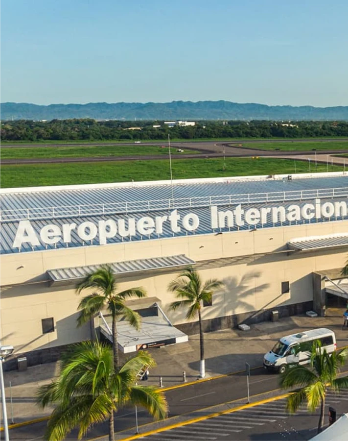 Edificio del aeropuerto con palmeras y pista al fondo.