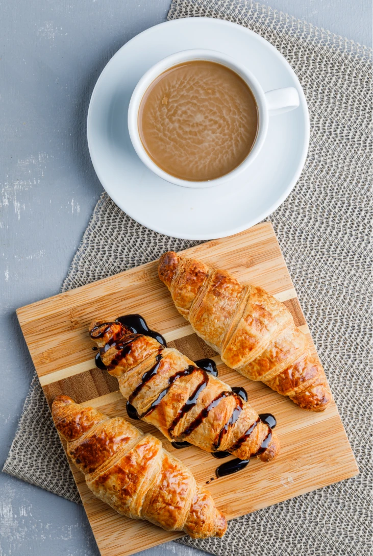 Croissants con chocolate y caf&eacute; sobre una tabla de madera.