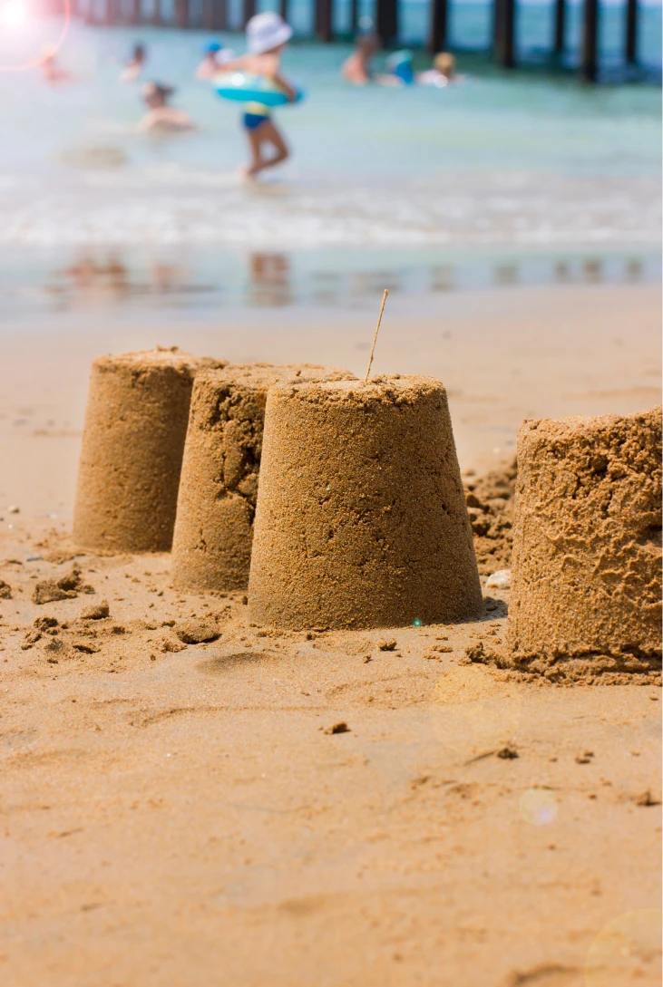 Castillos de arena en la playa con ni&ntilde;os jugando en el agua de fondo.