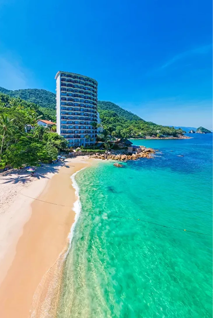 Hotel frente al mar con playa de arena y aguas turquesas.