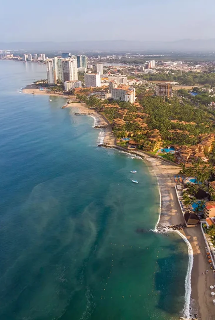 Vista a&eacute;rea de una costa con edificios y palmeras junto a un mar azul.
