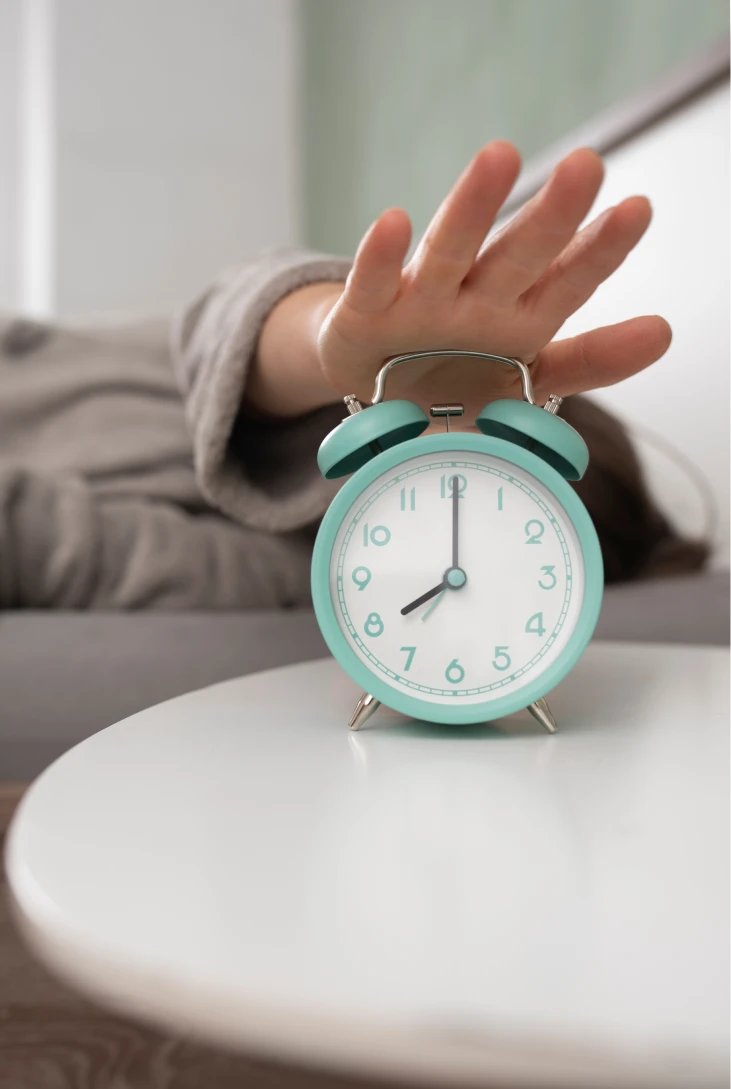 Mano alcanzando despertador azul pastel en la mesa.