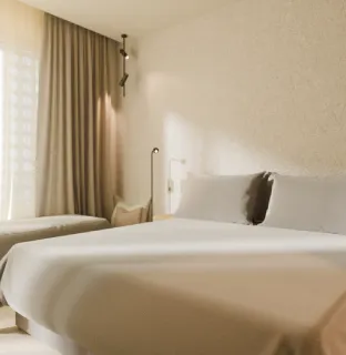 Habitaci&oacute;n de hotel con cama doble y suave iluminaci&oacute;n natural.