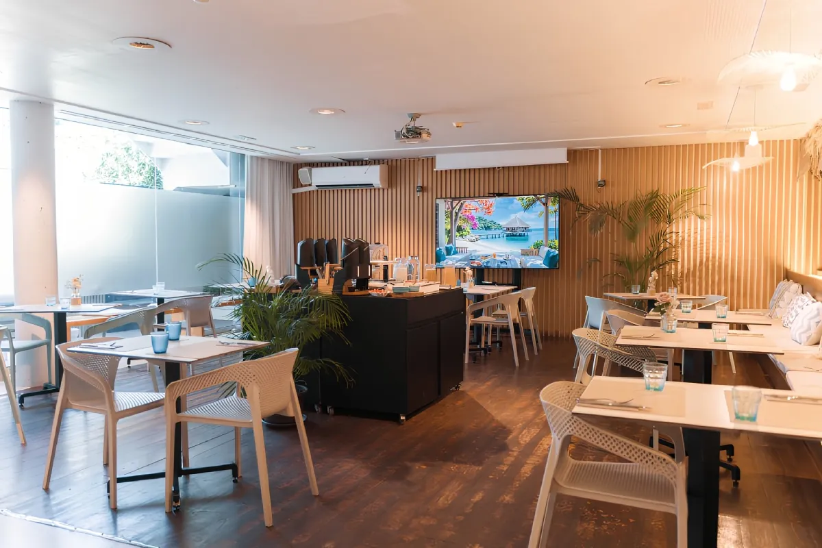 Restaurante moderno con mesas blancas y decoraci&oacute;n tropical.