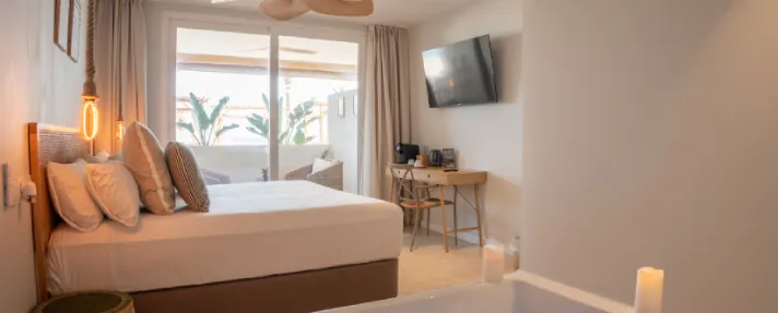 Habitaci&oacute;n moderna con cama, TV y balc&oacute;n con vista a las plantas.