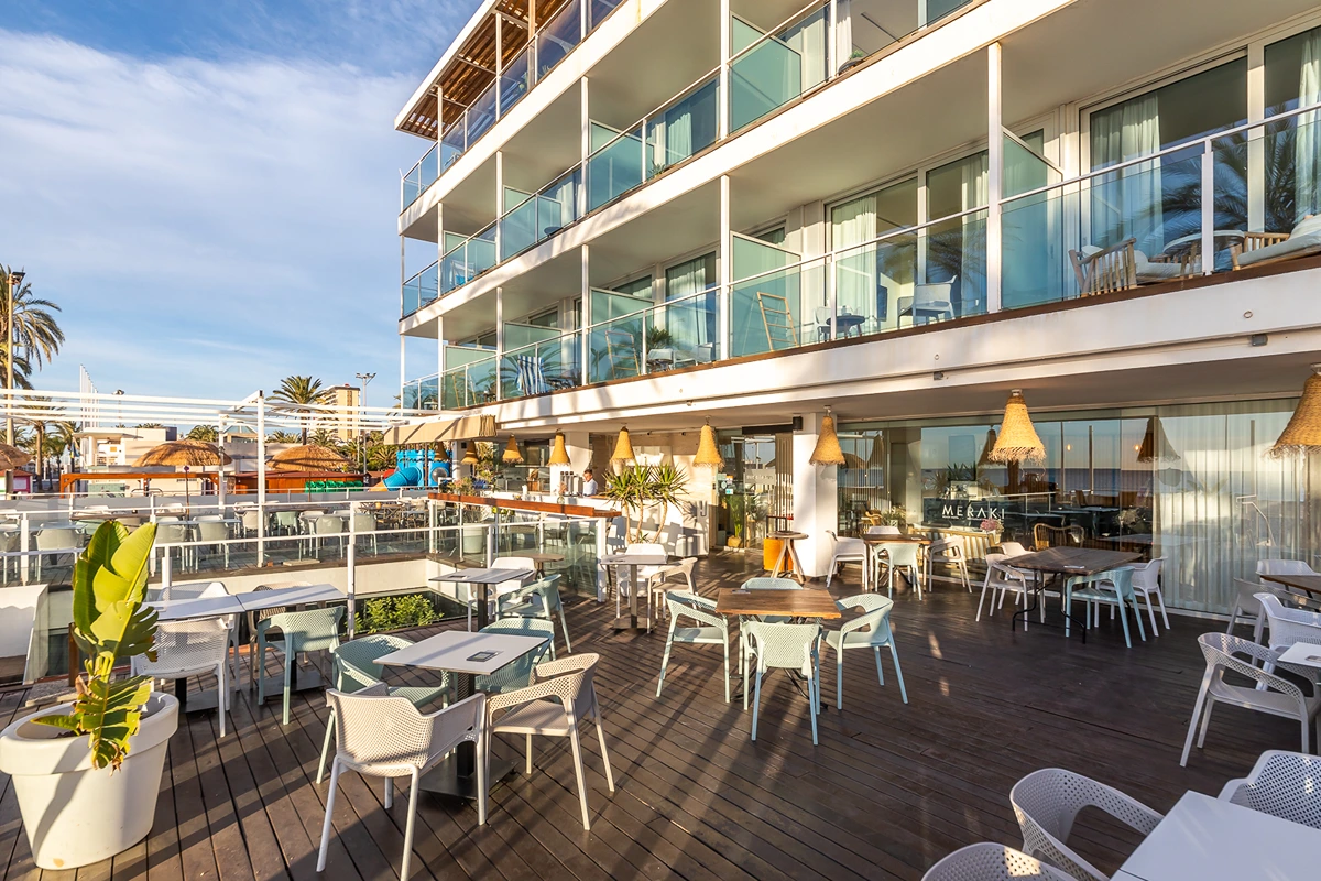 Terraza de restaurante con mesas y sillas al aire libre junto a un edificio moderno.
