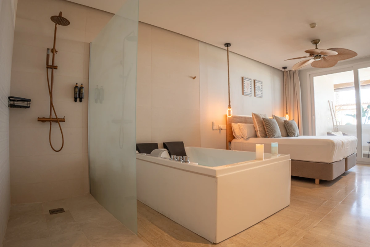 Dormitorio moderno con ba&ntilde;era, ducha y cama grande en tonos beige y blancos.