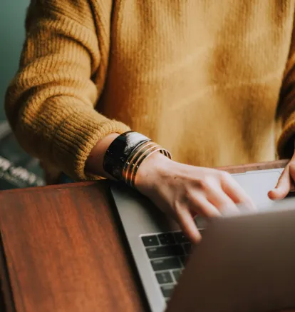 Persona escribiendo en una laptop con su&eacute;ter amarillo y brazalete llamativo.