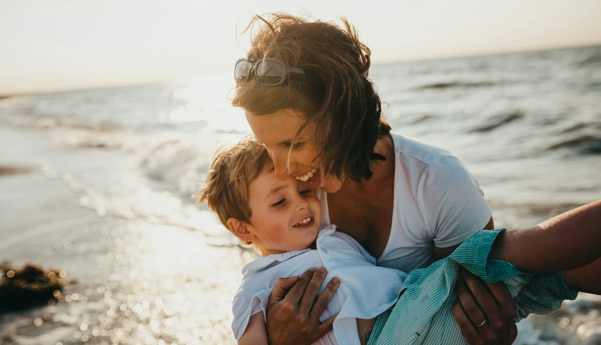 Madre e hijo sonr&iacute;en y juegan juntos en la playa al atardecer.