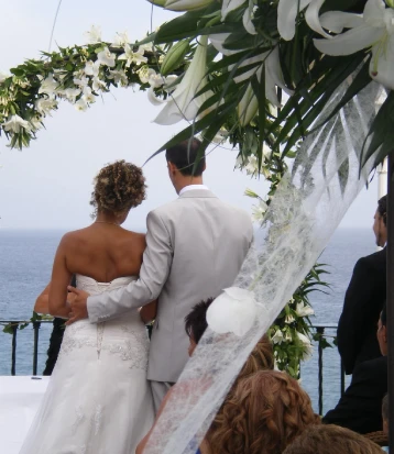 Pareja de novios frente al mar bajo un arco floral en su boda.