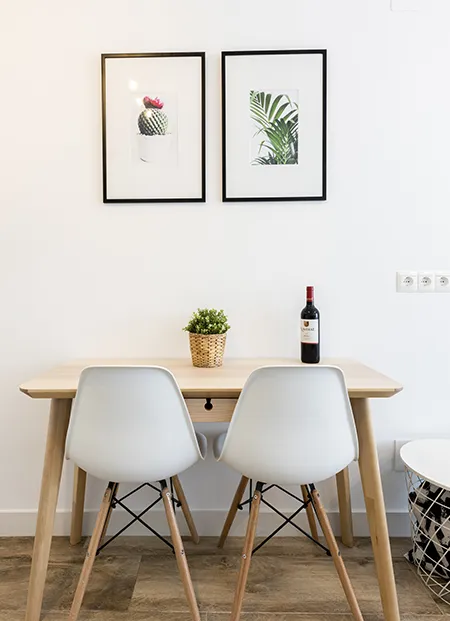 Mesa con sillas, vino, planta y cuadros de cactus y hojas.