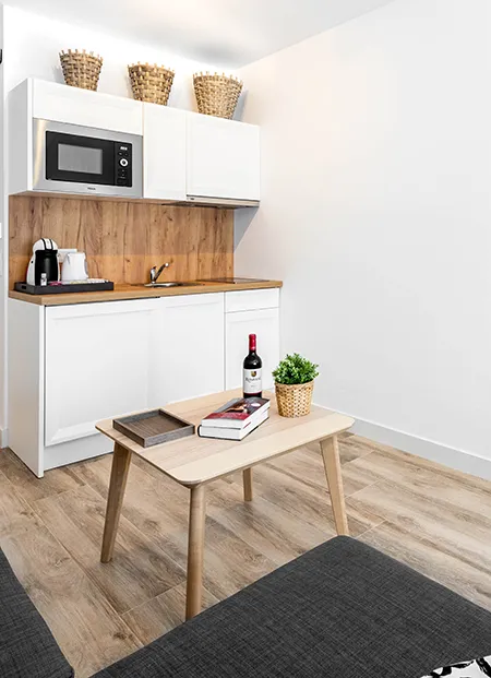 Cocina compacta con mesa, libros, vino y decoraci&oacute;n de plantas.
