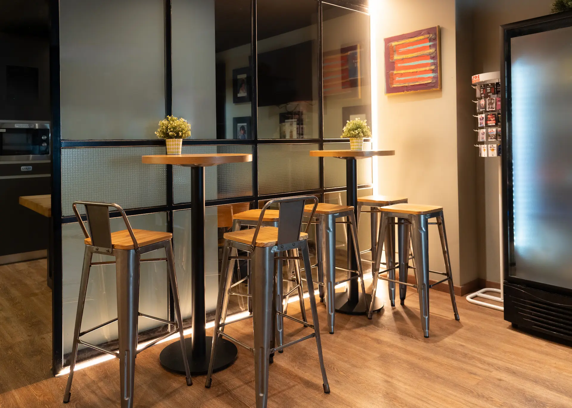 Mesas altas con sillas met&aacute;licas en una cafeter&iacute;a moderna.