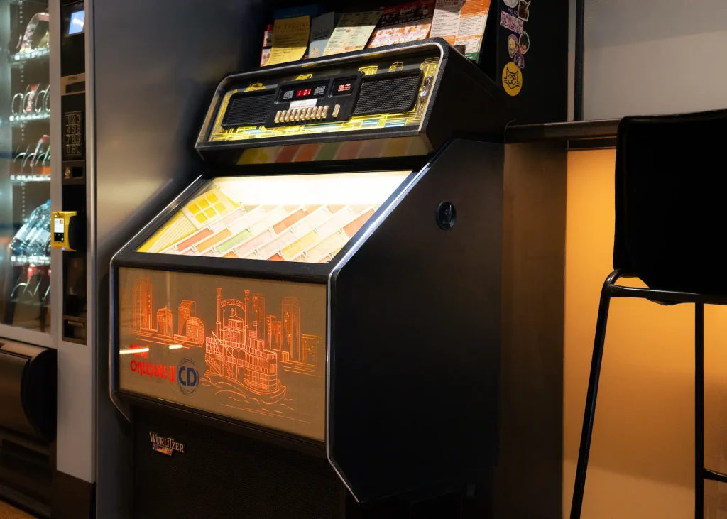Jukebox cl&aacute;sico junto a una m&aacute;quina expendedora, decorado con dise&ntilde;o urbano.