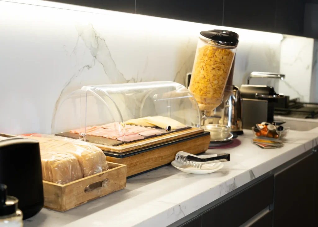 Buffet con pan, fiambres y cereales en una encimera blanca.