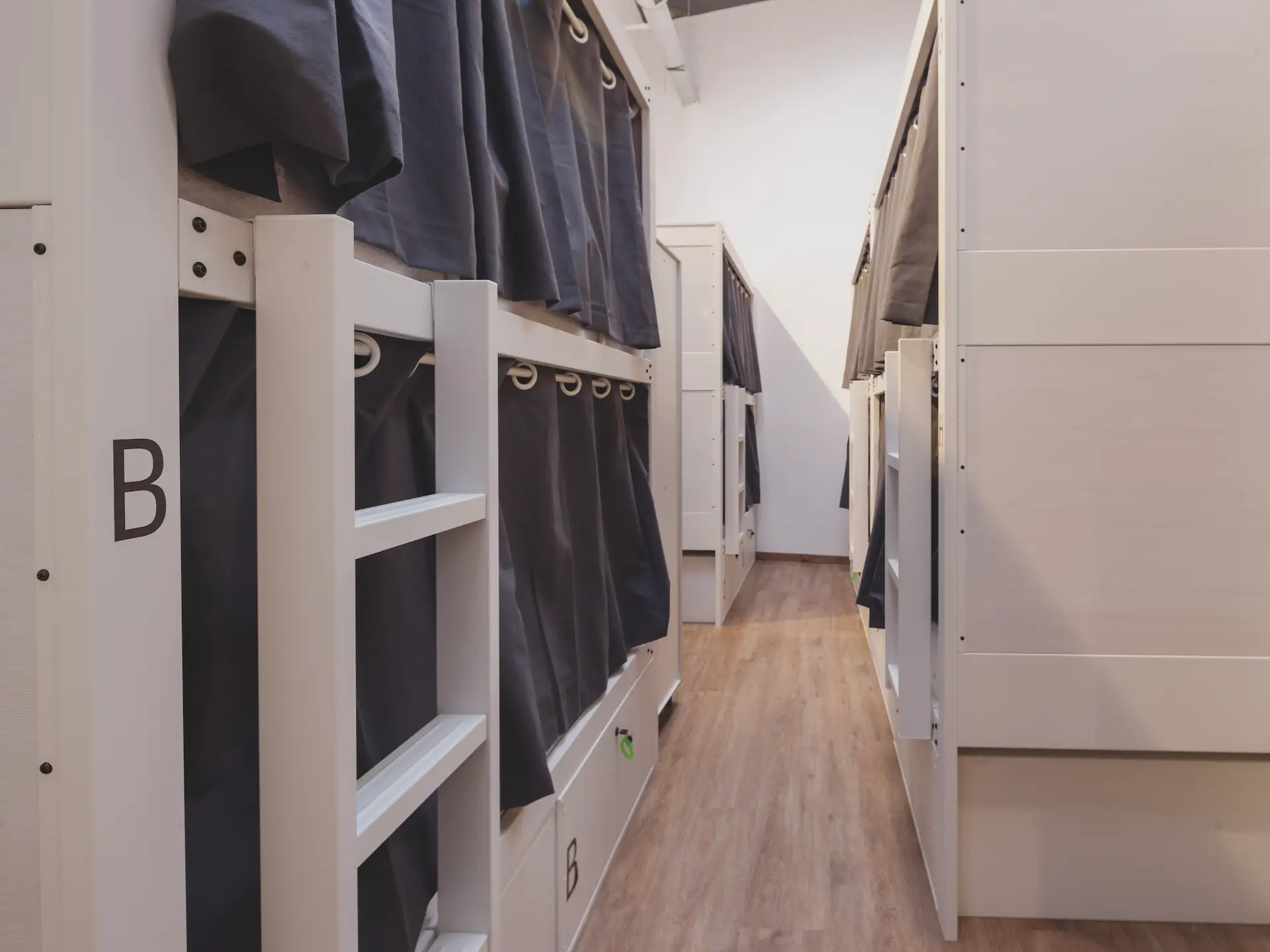 Pasillo de literas con cortinas oscuras en un dormitorio compartido.