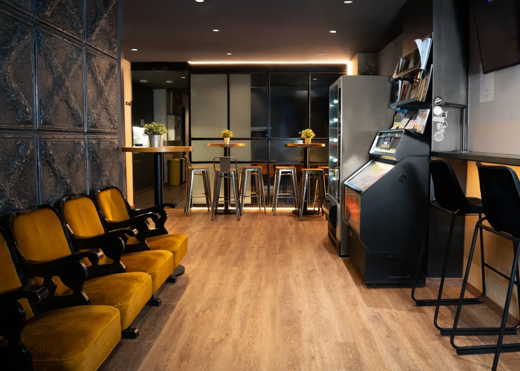 Sala moderna con sillas, mesas altas, m&aacute;quina expendedora y decoraciones verdes.
