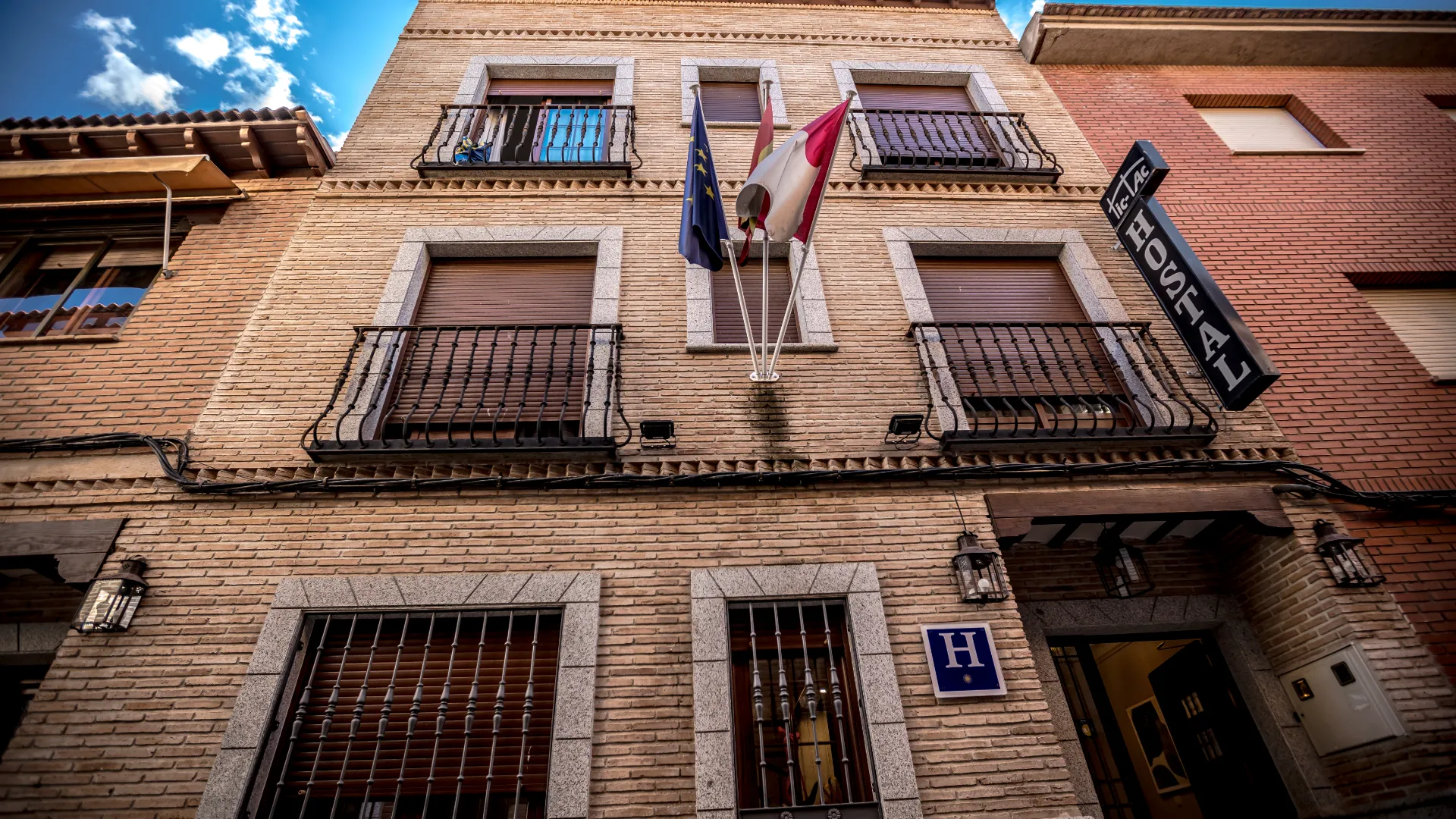 Fachada de un edificio de ladrillo con balcones, banderas y un letrero de "Hostal".