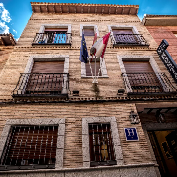 Fachada de hotel de ladrillo con banderas y signo de "H" azul en la entrada.