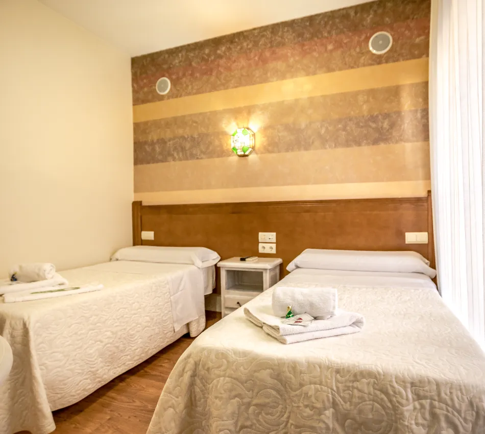 Habitaci&oacute;n con dos camas individuales, decorada en tonos c&aacute;lidos, con l&aacute;mpara de pared.