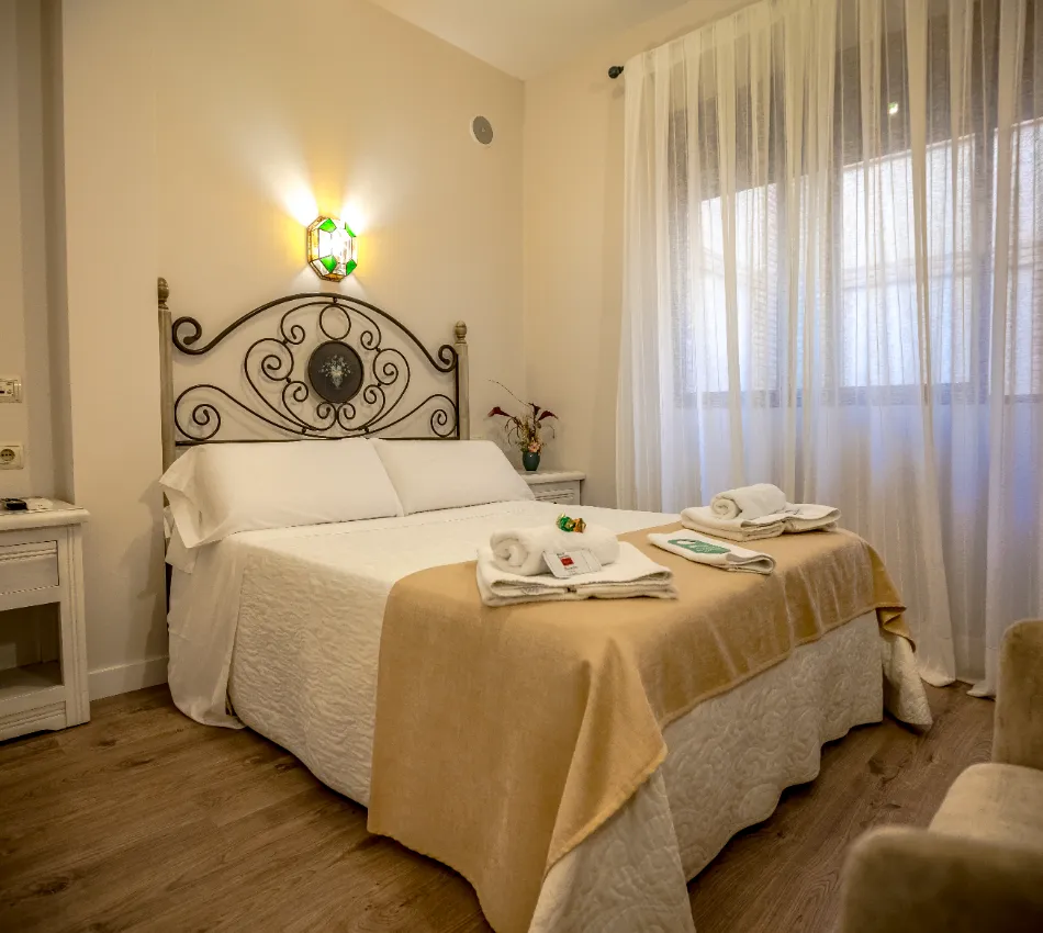 Habitaci&oacute;n con cama matrimonial, cabecero decorativo y luz tenue.