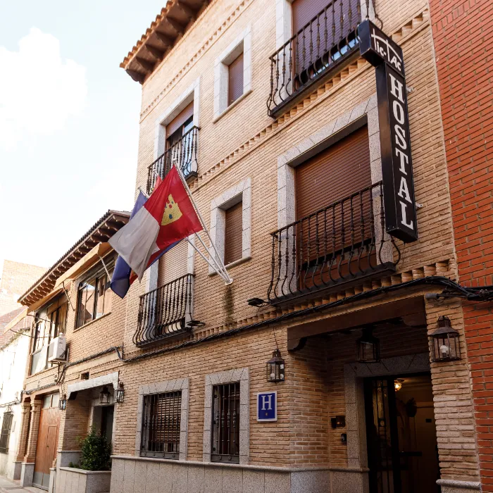Fachada de un hostal de ladrillos, con balcones y banderas ondeando junto a la entrada.