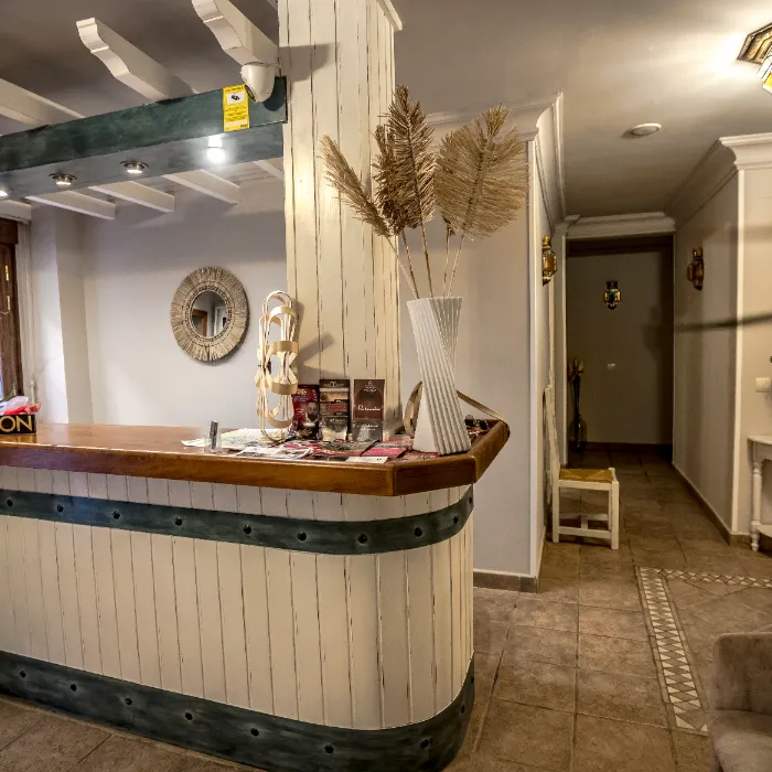 Recepci&oacute;n de hotel con decoraci&oacute;n r&uacute;stica y jarr&oacute;n con hojas secas. Pasillo al fondo.