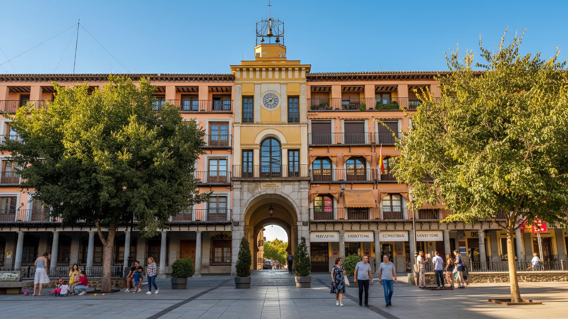 Personas caminando por una plaza con un edificio de reloj en el fondo, rodeado de &aacute;rboles.
