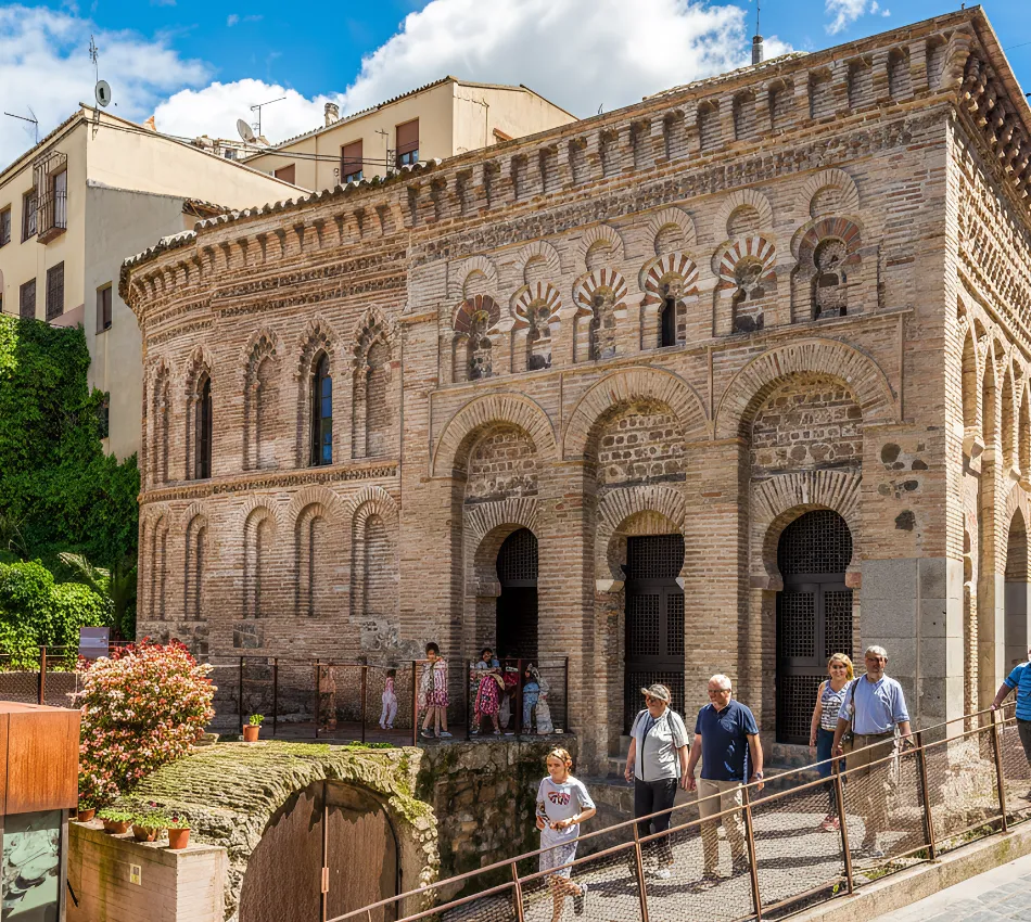 Edificio hist&oacute;rico de ladrillo con arcos y detalles decorativos; varias personas caminando afuera.