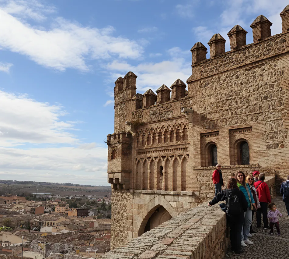 Un grupo de personas junto a una muralla medieval, con una ciudad al fondo bajo un cielo azul.