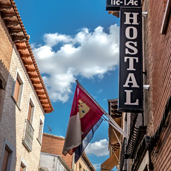 Calle con cartel de "Hostal", bandera y cielo azul con nubes.