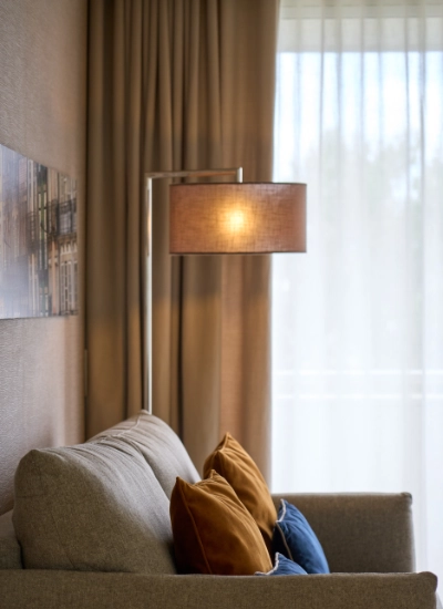 Sala com sof&aacute; cinza, almofadas coloridas e lumin&aacute;ria ao lado.