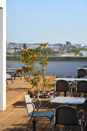 Terra&ccedil;o com mesas ao ar livre, vista para cidade e rio ao fundo.