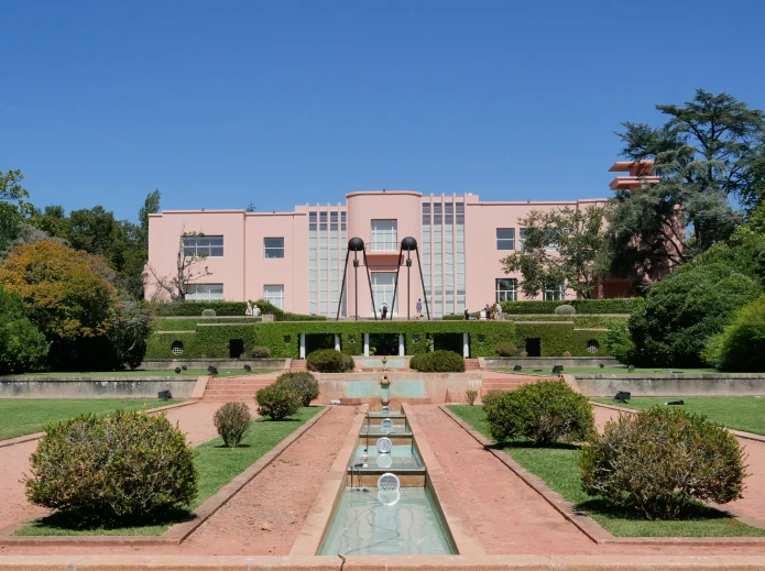 Edif&iacute;cio rosa com jardim e fonte em um dia ensolarado.
