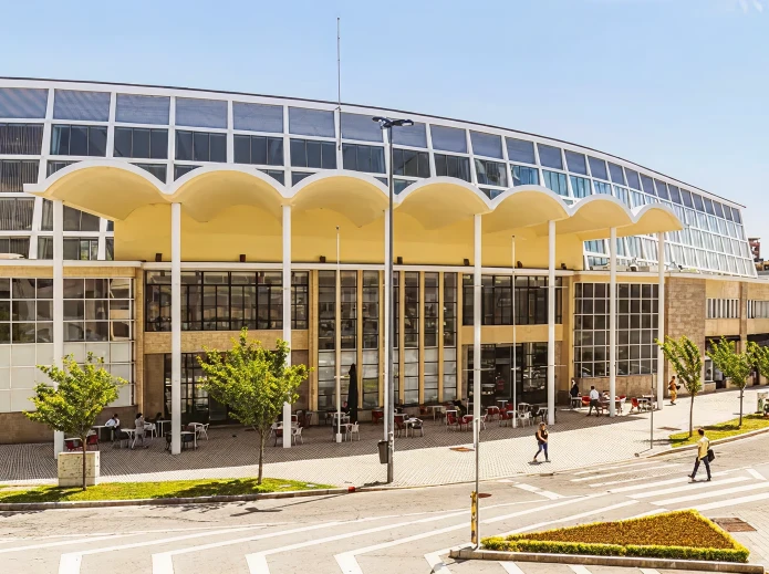 Pr&eacute;dio moderno com fachada curva e colunatas amarelas em dia ensolarado.