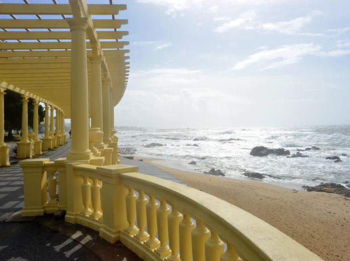 Cal&ccedil;ad&atilde;o &agrave; beira-mar com p&eacute;rgula amarela sob c&eacute;u claro.