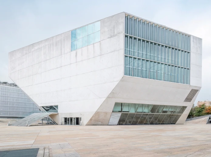 Edif&iacute;cio moderno com fachada angular e vidro, c&eacute;u claro ao fundo.