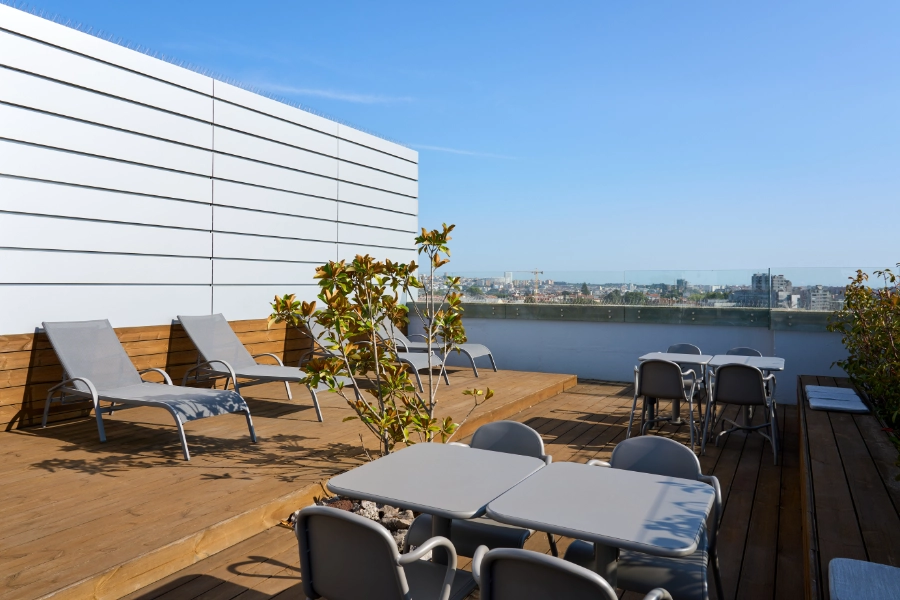 Terra&ccedil;o com espregui&ccedil;adeiras, mesas, cadeiras e vista da cidade.