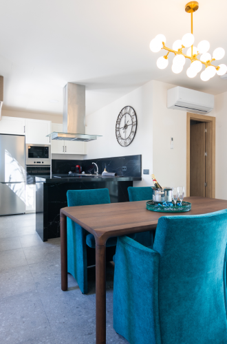 Comedor moderno con sillas turquesas y cocina al fondo.