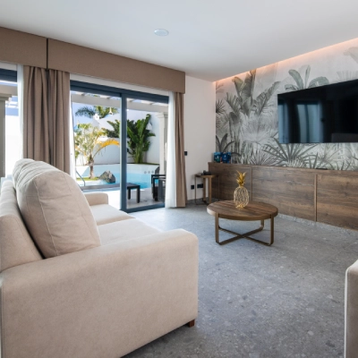 Sala moderna con sof&aacute; beige, mesa redonda y vista a una piscina exterior.
