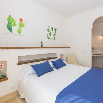 Habitaci&oacute;n moderna con cama, cojines azules y decoraciones de cactus en la pared.