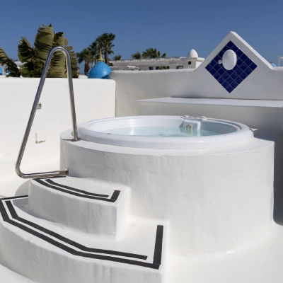 Jacuzzi blanco al aire libre con escaleras en un entorno soleado y moderno.