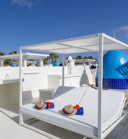 Cama balinesa blanca con dos sombreros en un entorno soleado.