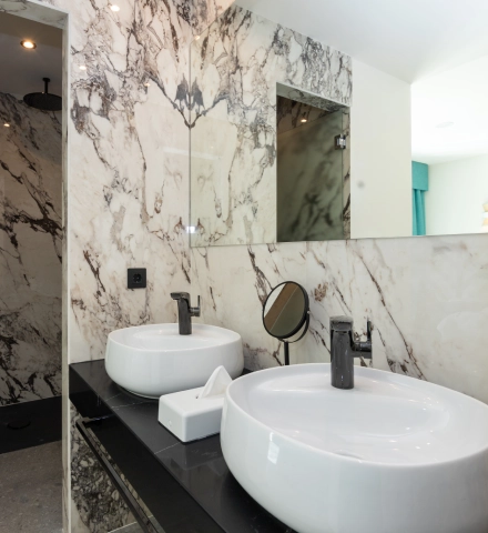 Ba&ntilde;o moderno con dos lavabos y paredes de m&aacute;rmol.